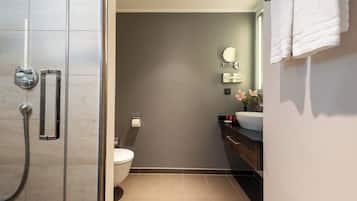 A modern bathroom with a glass shower enclosure, a toilet, a sink, and a mirror.