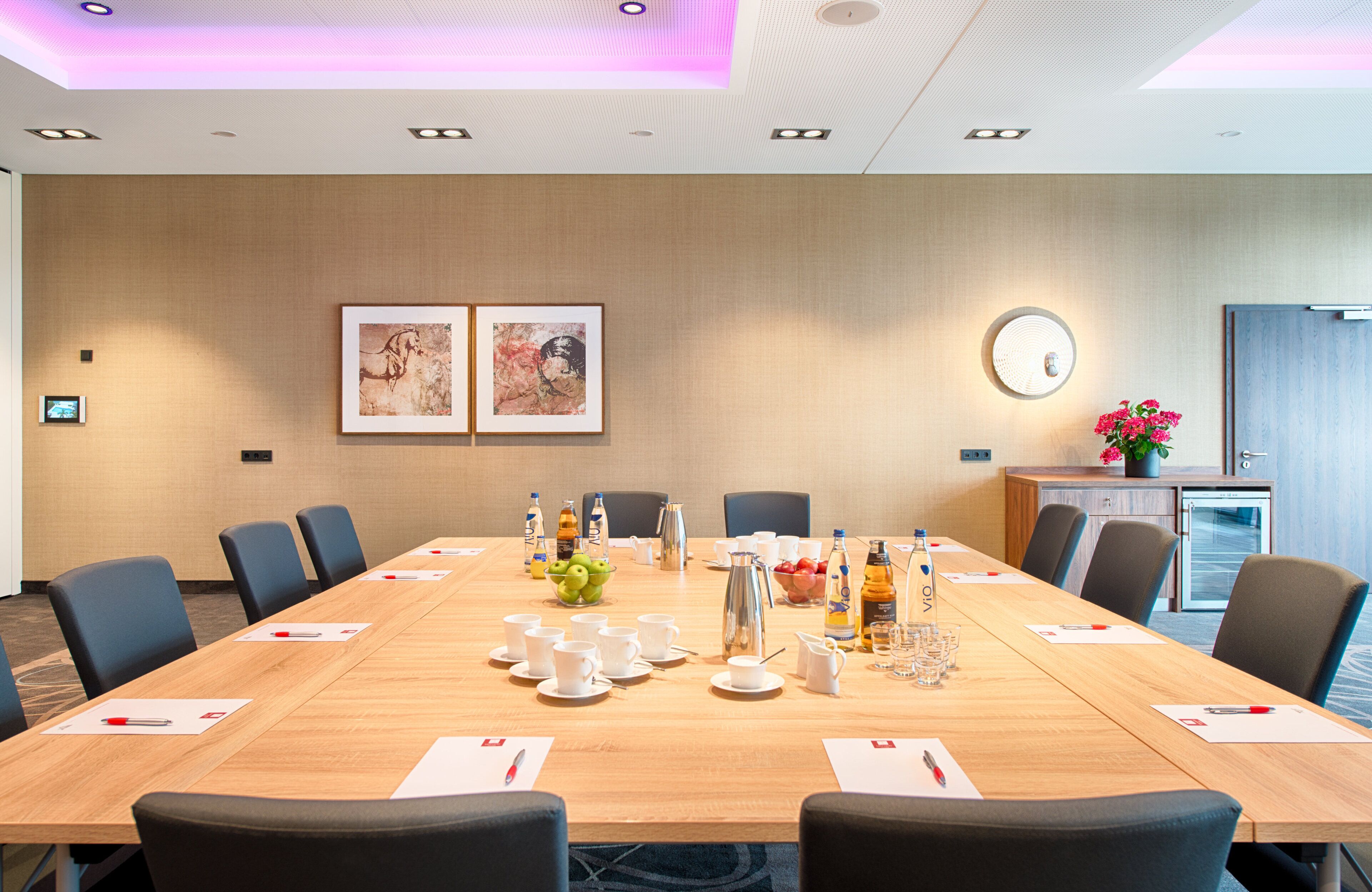 A conference room with a long table, chairs, and various amenities like a coffee station and a fruit bowl.