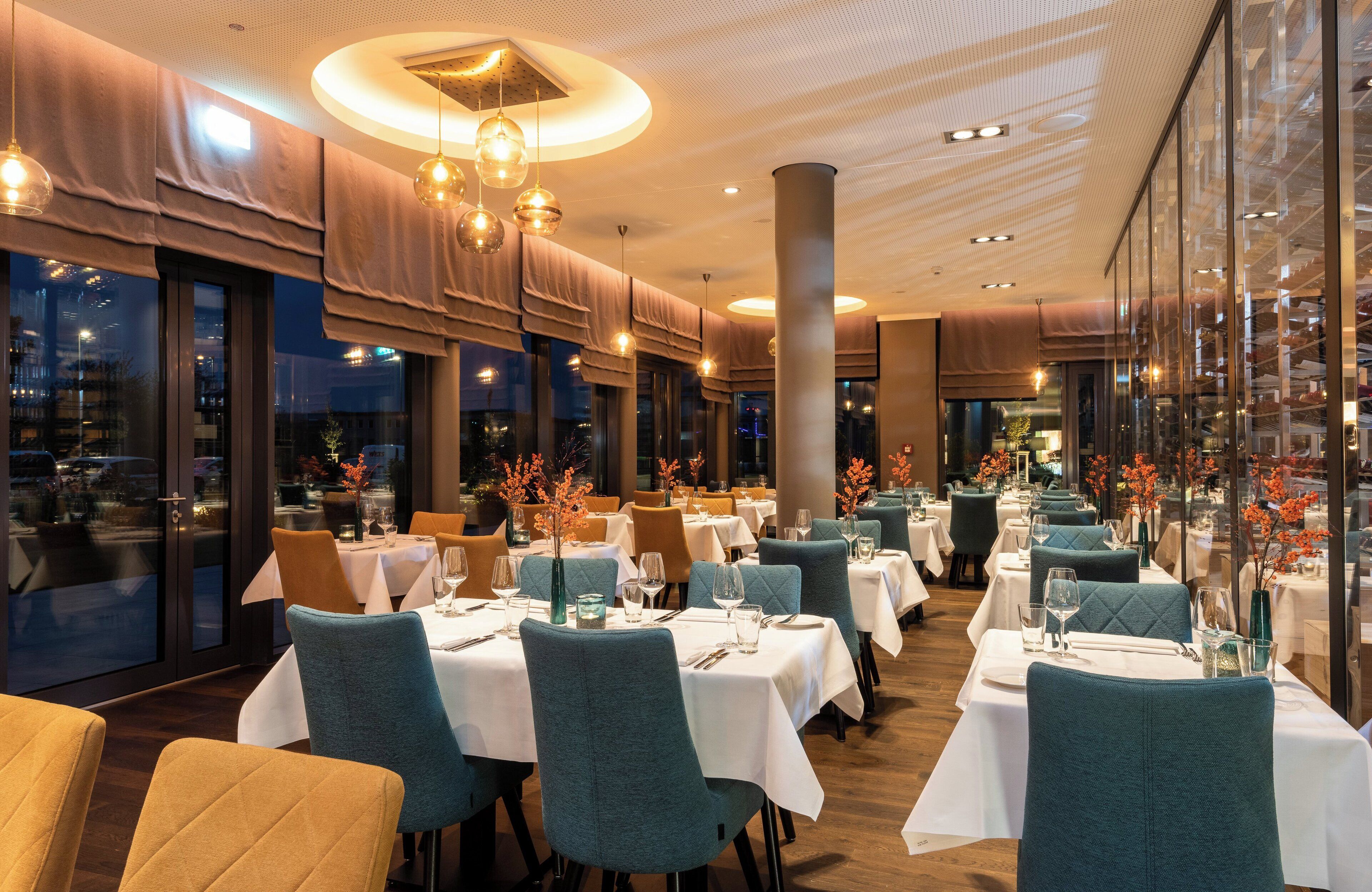 Ein Restaurant mit mehreren Tischen, Stühlen und einem modernen Deckenstil.