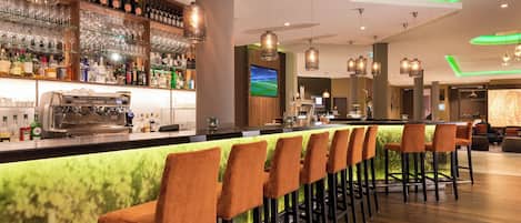A bar area with a long counter, multiple bar stools, and a variety of bottles and glasses.
