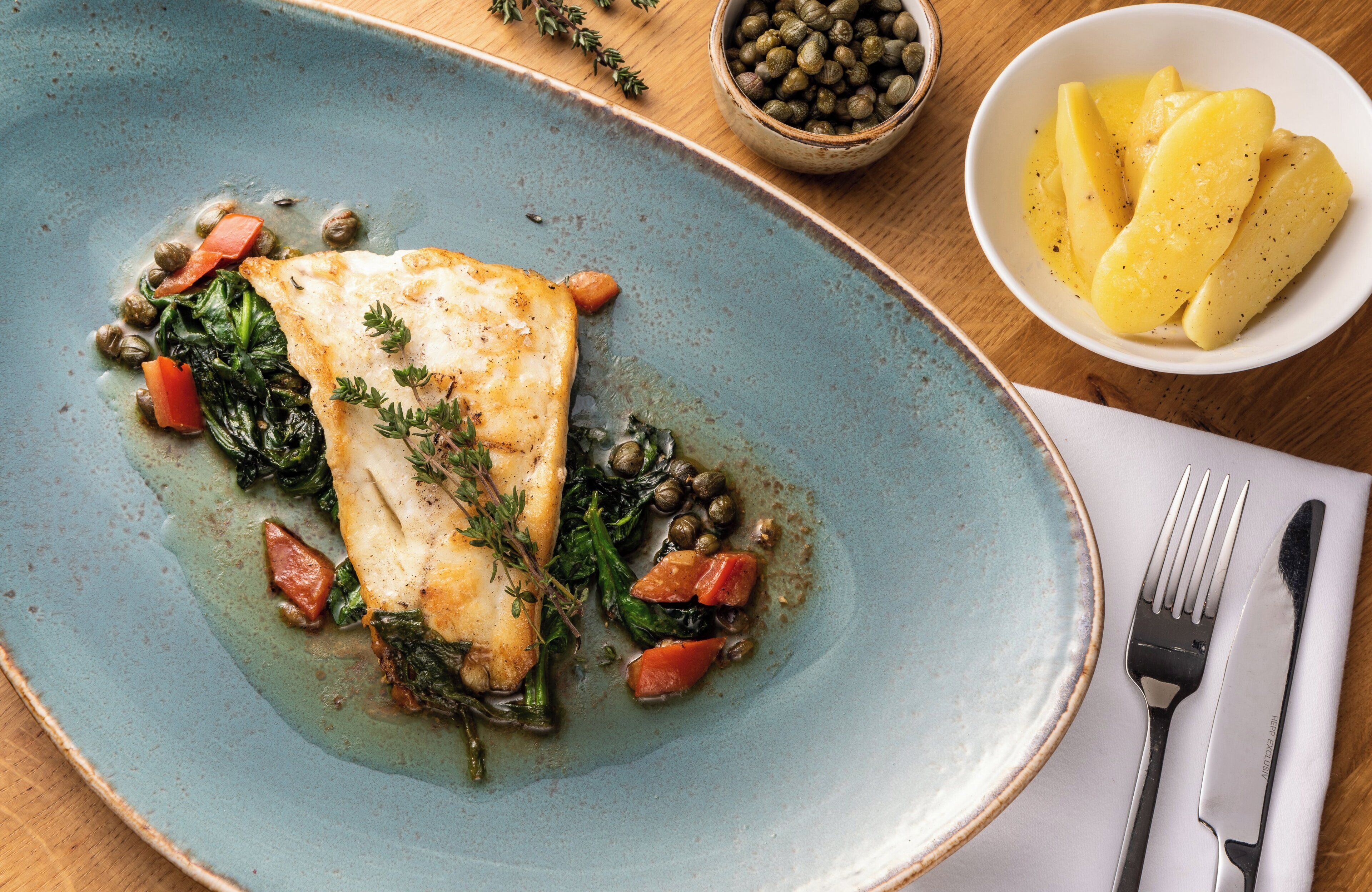 Prato de comida com filé de peixe, legumes e alcaparras.