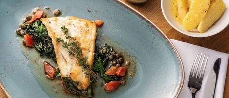 Prato de comida com filé de peixe, legumes e alcaparras.
