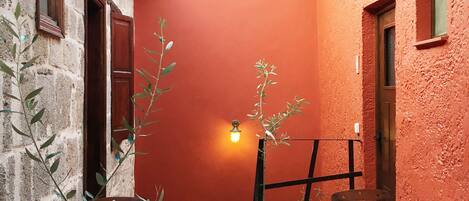 A narrow courtyard with red walls, two white tables, and wooden chairs.