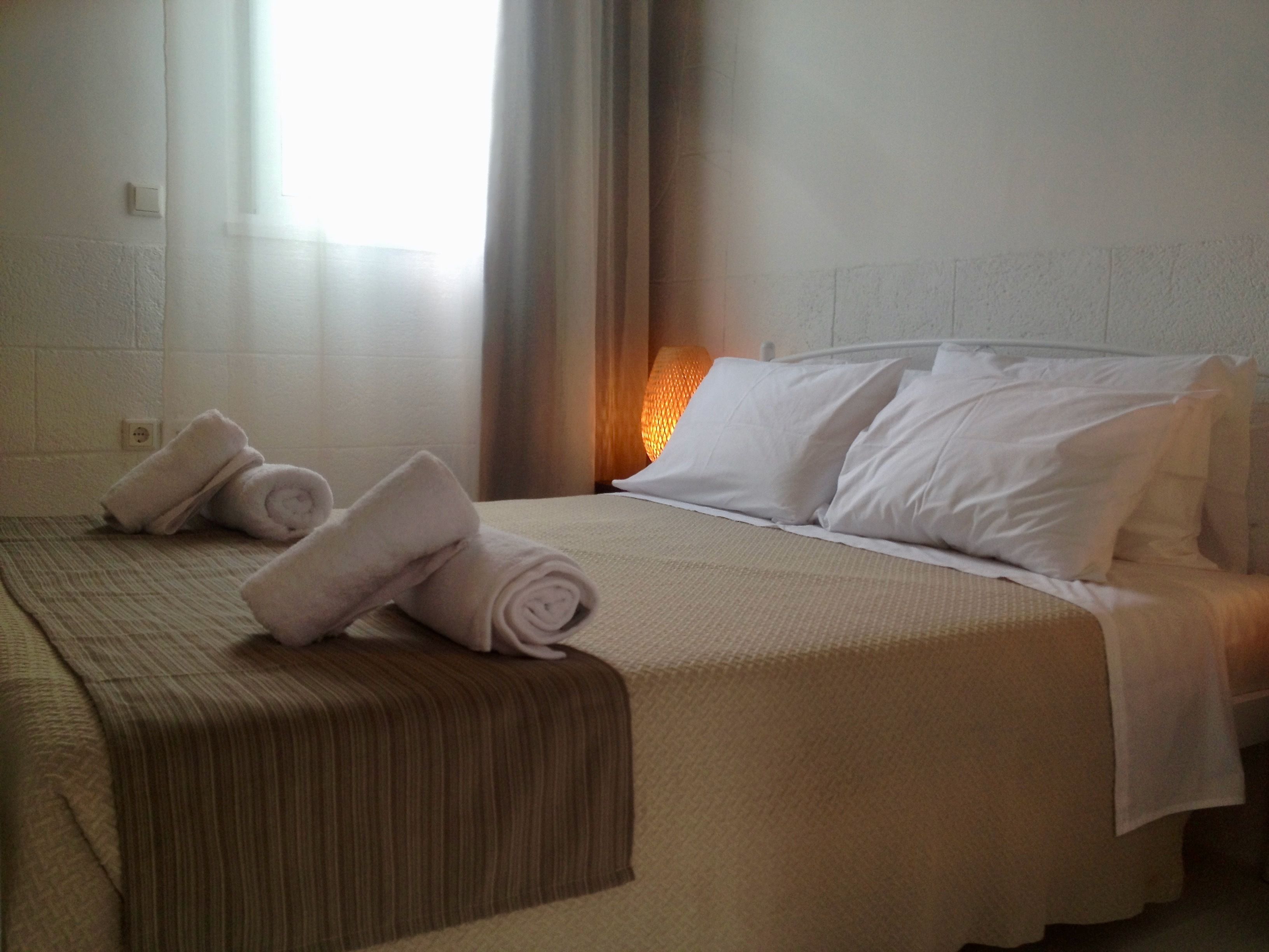 Een hotelkamer met een net opgemaakt bed, een bedlampje en een raam met gordijnen.