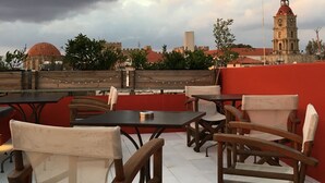 An outdoor seating area with tables and chairs, overlooking a cityscape with a prominent tower. - Auberge 32 | Old Town (Rhodes)