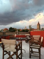 Egy szabadtéri ülőhely, ahol asztalok és székek állnak, és ahonnan a városra nyílik kilátás, melyben egy feltűnő torony is látható.