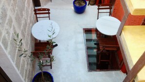 A small outdoor patio with two round tables and two chairs, surrounded by potted plants and a red wall. - Auberge 32 | Old Town (Rhodes)