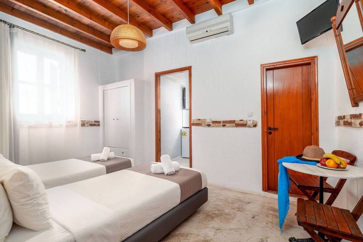 A bedroom with two beds, a small table with fruits, a TV, and a wooden ceiling.