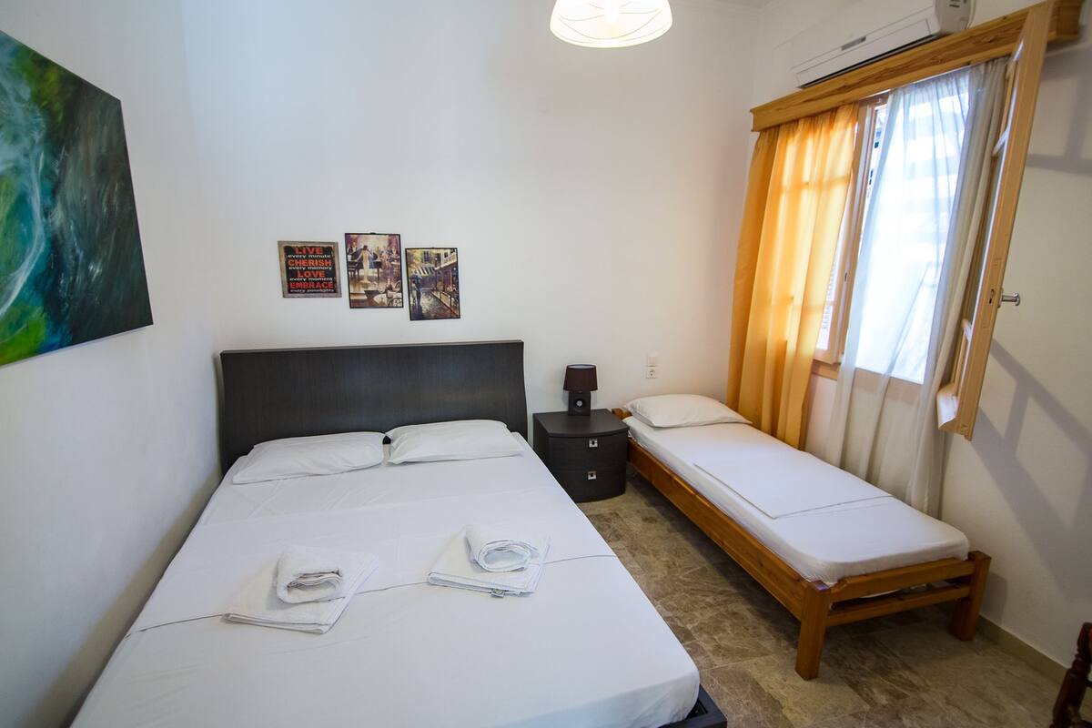 Hotellihuone, jossa on suuri sänky, pienempi sänky, yöpöytä ja ikkuna, jossa on verhot.