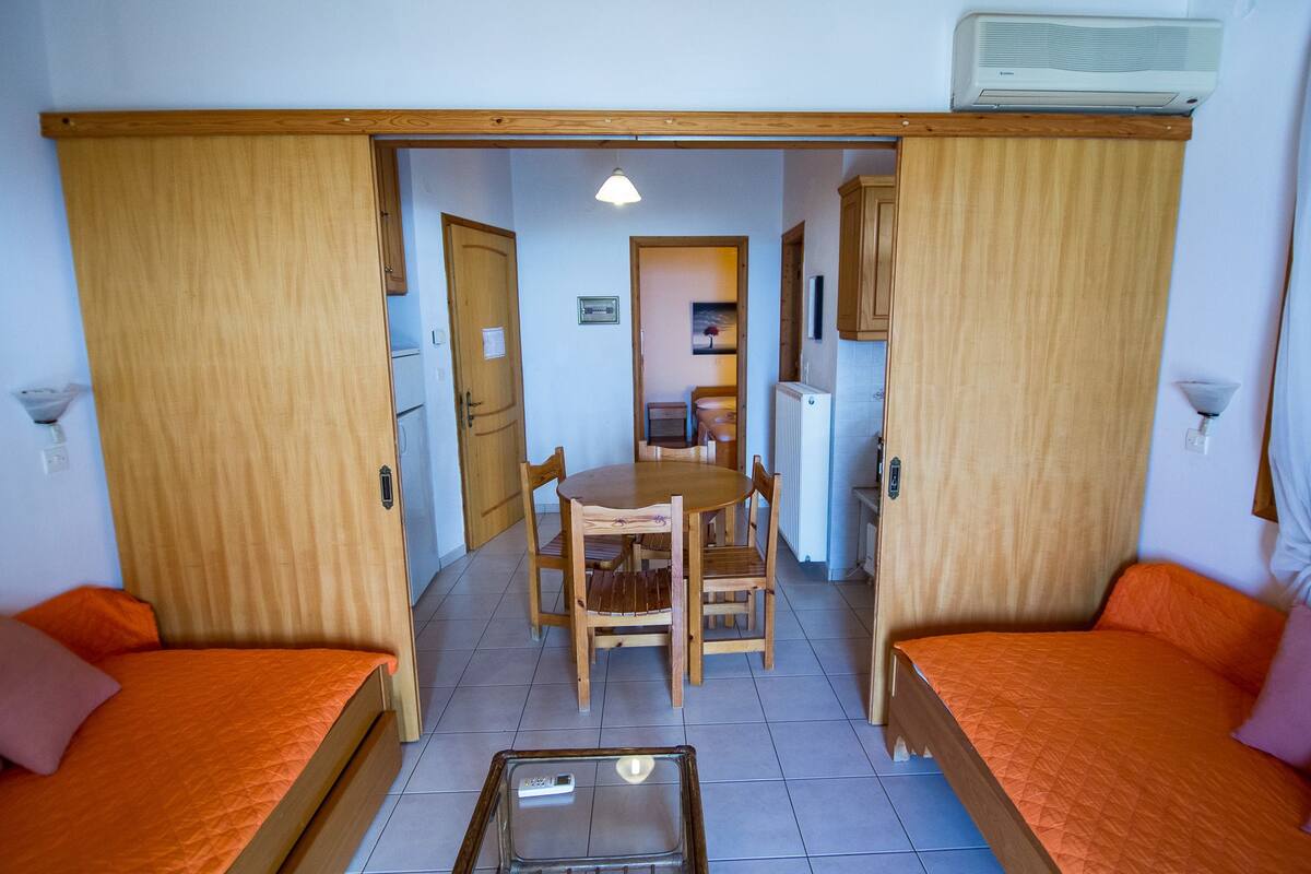 Kompakti huone, jossa on kaksi erillistä sänkyä, pieni ruokapöytä ja pieni keittiönurkkaus.