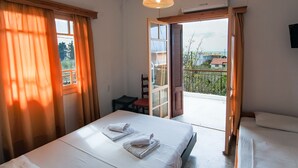 A hotel room with a bed, a chair, a table, and a balcony with a view of buildings and trees. - Margarita Apartments (Preveza)