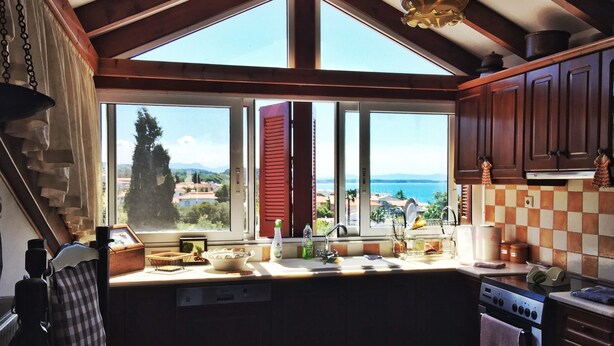 A kitchen with a view of the sea, wooden cabinets, and a window with shutters. - Margarita Apartments (Preveza)