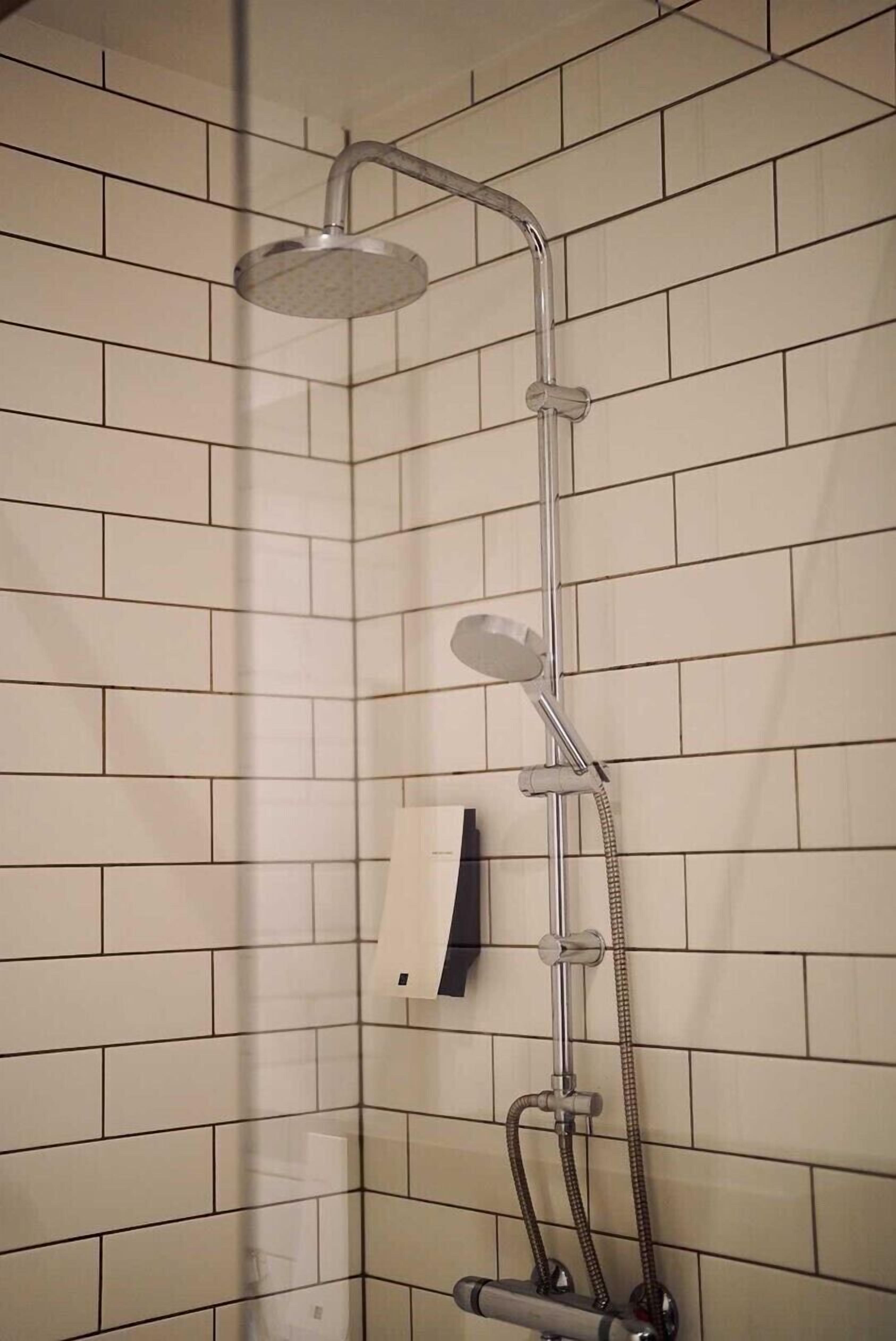 A shower with a handheld showerhead and a handheld shower attachment, mounted on a tiled wall.