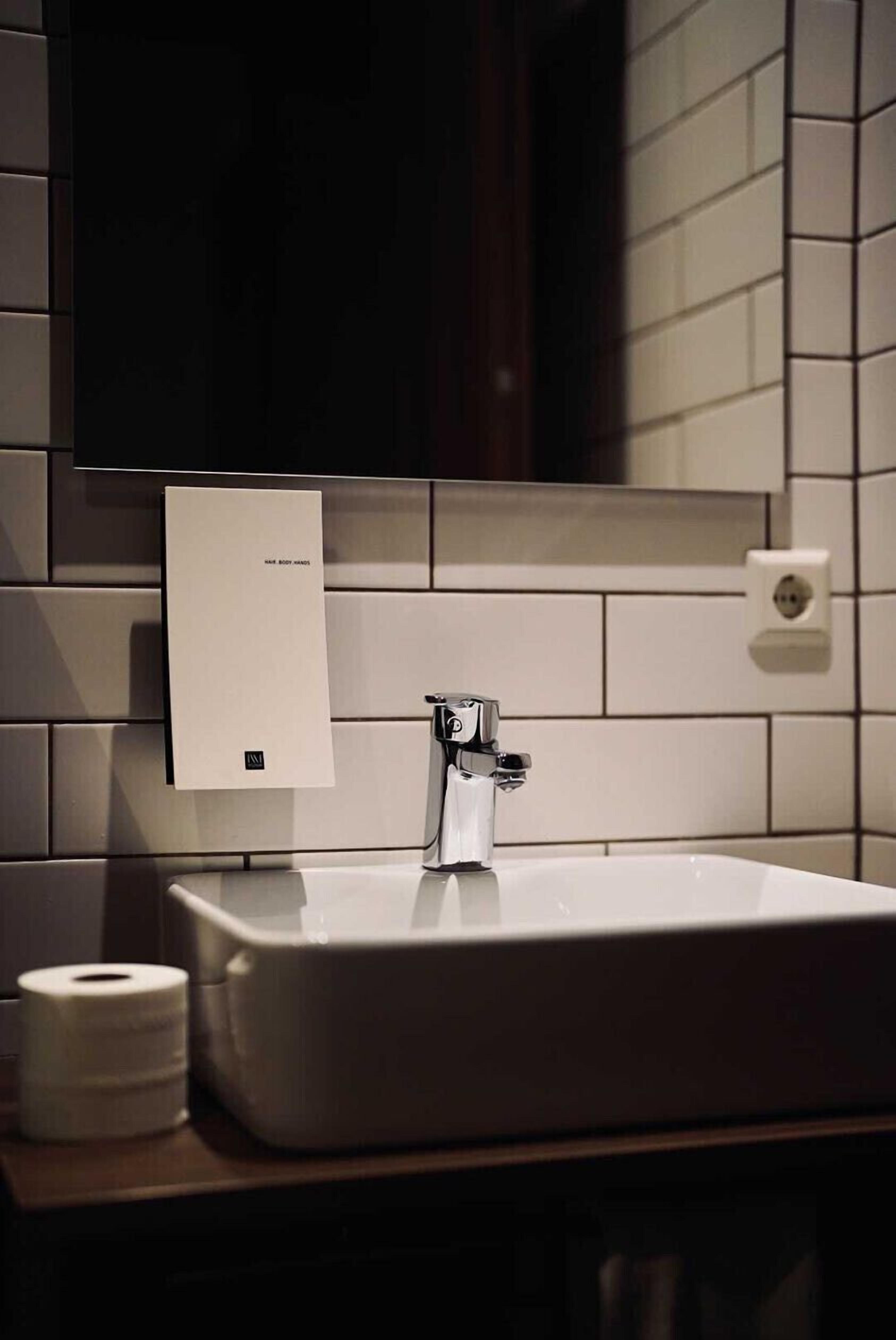 Une salle de bain avec un lavabo blanc, un miroir et un distributeur de serviettes en papier.