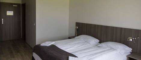 A hotel room with a double bed, wooden flooring, a wardrobe, and a bedside table with a lamp.