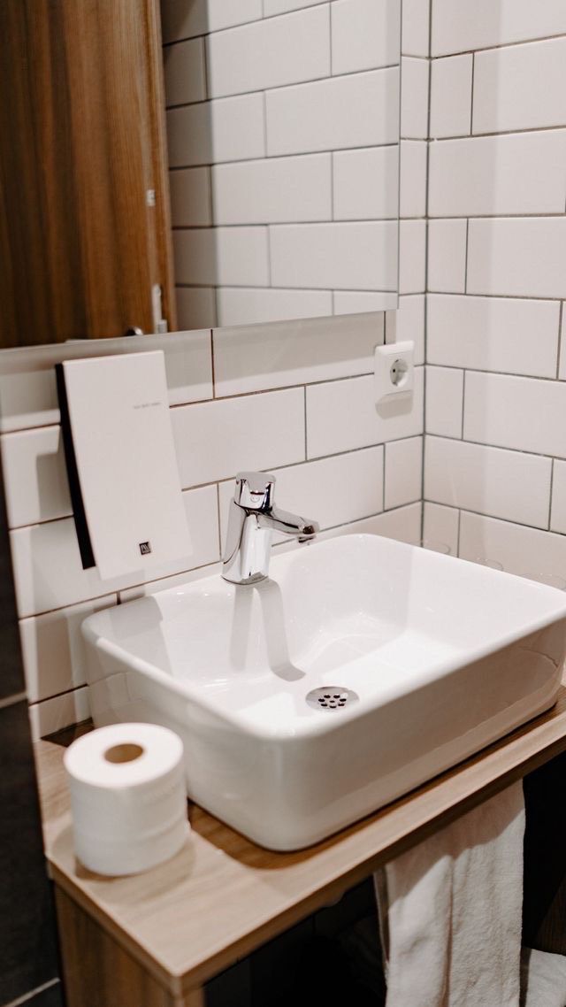 Et badeværelse med en hvid vask, et spejl og et toiletpapirrulle på en træbordplade.