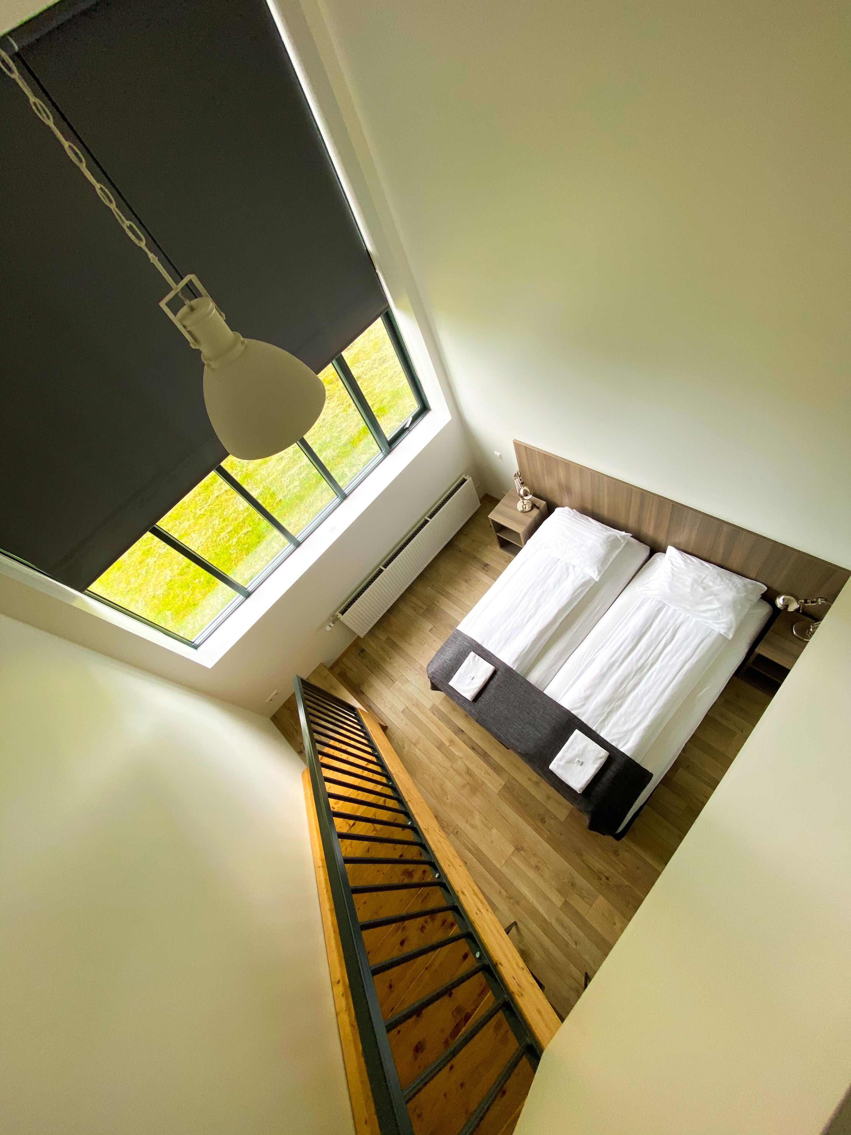 A bedroom with a large window, a wooden staircase, and a bed with white bedding.