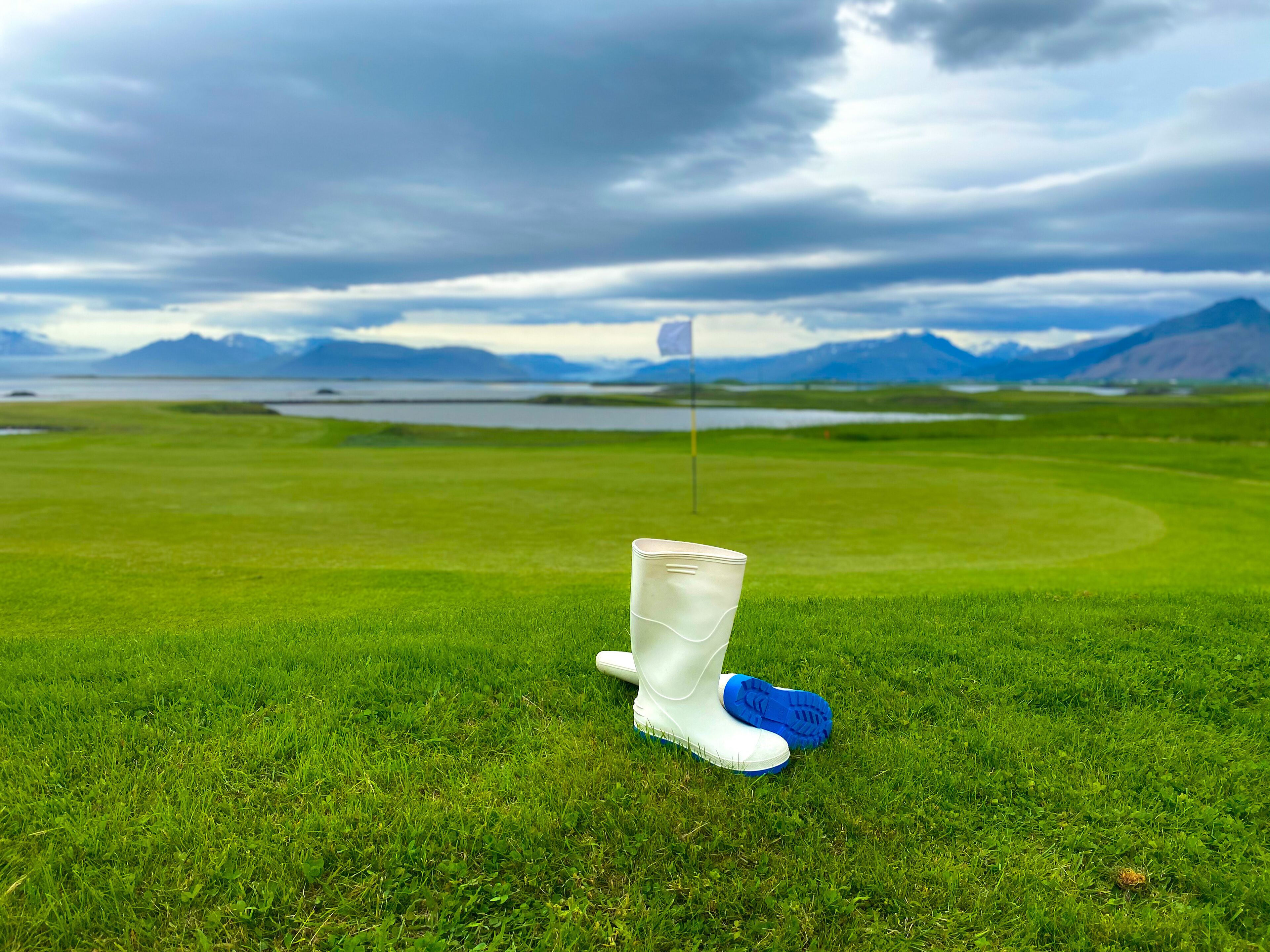 A golf course with a flagstick, a pair of golf shoes, and a water bottle on the grass.