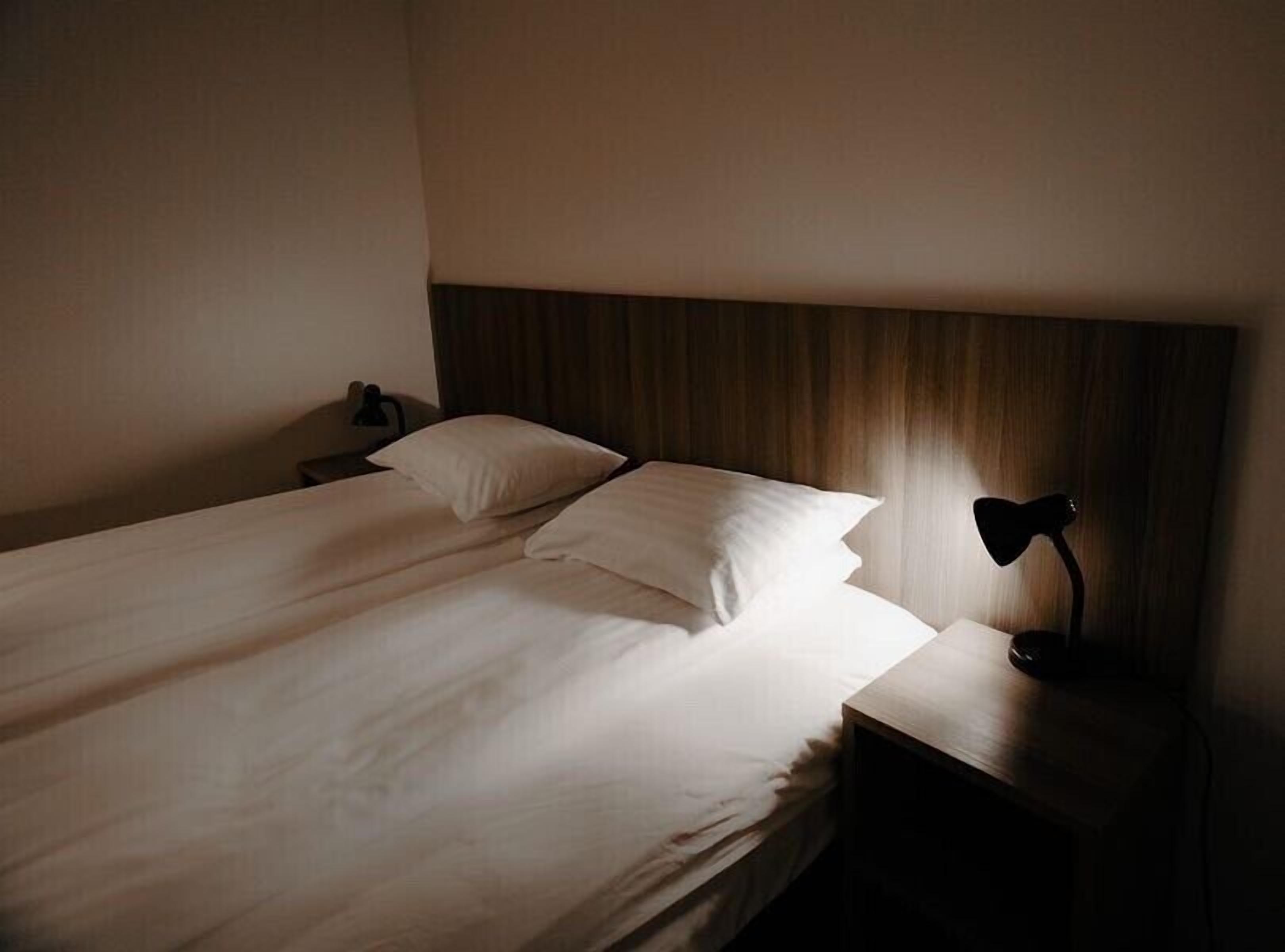 Un lit simple avec du linge de lit blanc dans une chambre d’hôtel.