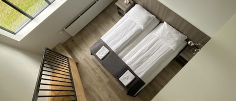 A bedroom with a bed, a nightstand, a window, and a wooden staircase.