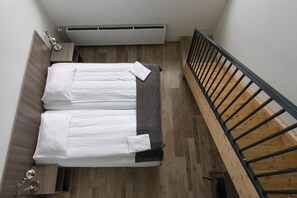 A bedroom with a bed, a radiator, a wooden floor, and a staircase.