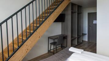 Une chambre avec un escalier en bois, un bureau, une chaise, un lit et des étagères intégrées.