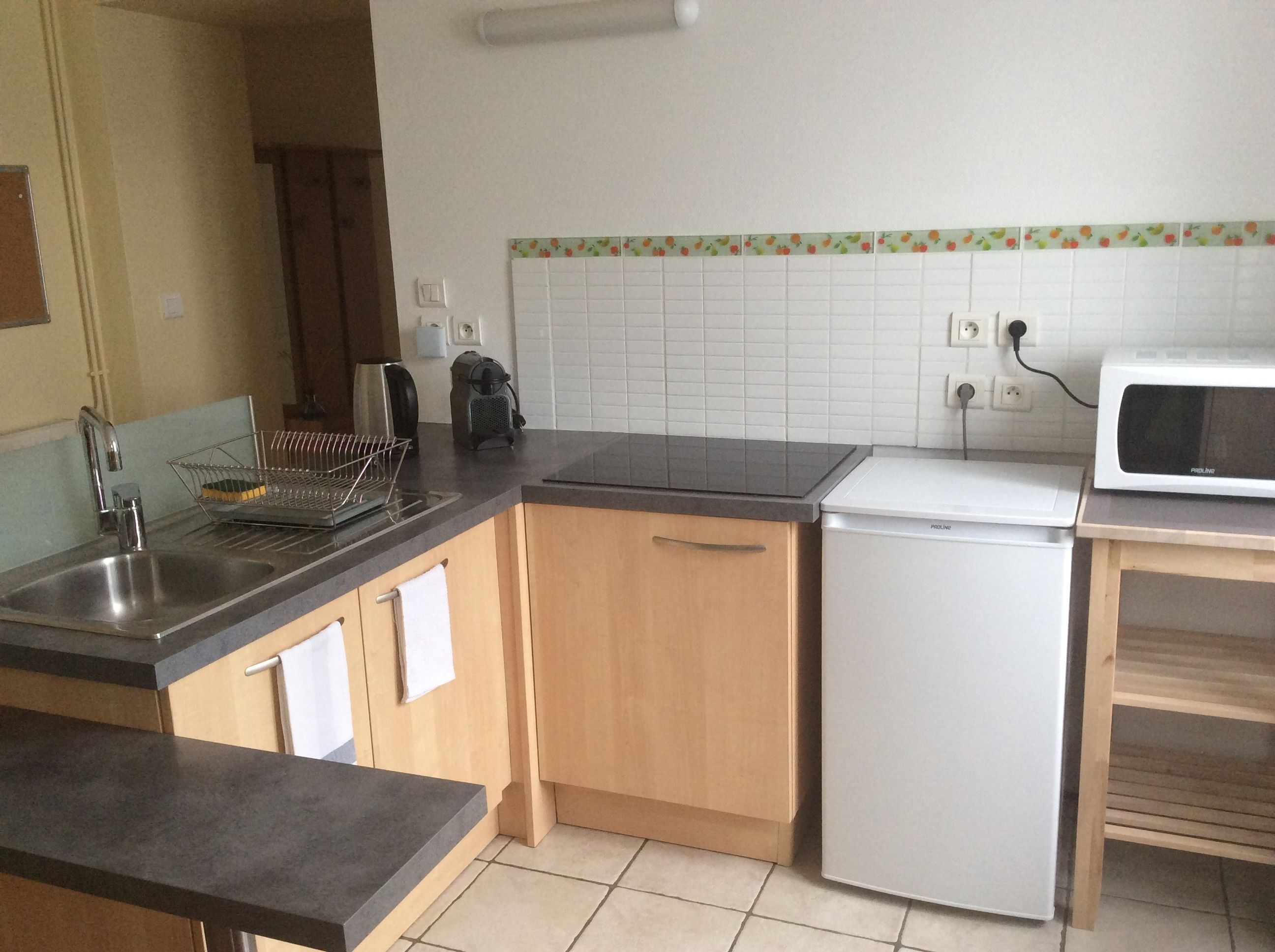 Una cocina compacta equipada con un lavamanos, un microondas, un refrigerador pequeño y un tostador.