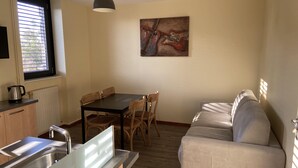 A compact kitchen with a dining area, a sofa, and a painting on the wall.