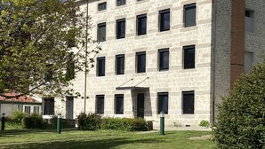 A multi-story building with a stone facade, multiple windows, and a small garden area in front.