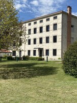 Un edificio de varios pisos con fachada de piedra, numerosas ventanas y un pequeño jardín delantero.