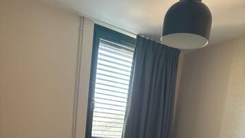 A bedroom with a bed, a window with curtains, a radiator, and a lamp.