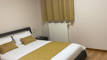 A neatly made bed with a white and mustard-colored bedspread, a black headboard, and a wooden floor.