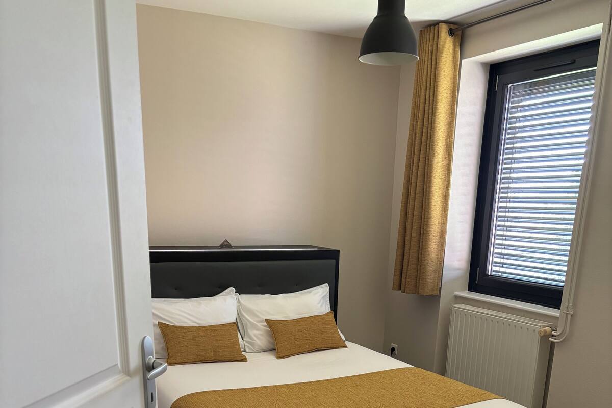 Une chambre à coucher avec un lit, une fenêtre avec des stores, un radiateur et une porte.