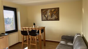 A modern living room with a wooden dining table, four chairs, a grey sofa, and a world map artwork on the wall.