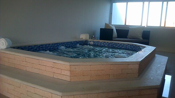 Un espace bien-être comprenant un bain à remous et un coin salon avec un canapé et des coussins.
