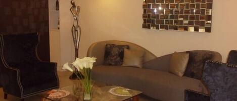 A modern living room with a glass coffee table, a sofa, and two armchairs.