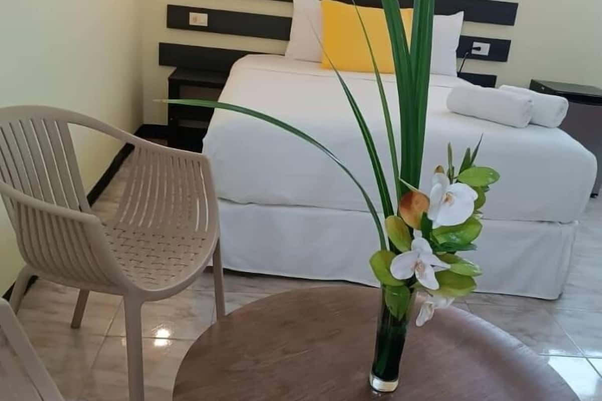 A hotel room with a bed, a bedside table with a vase of flowers, a chair, and a small table.