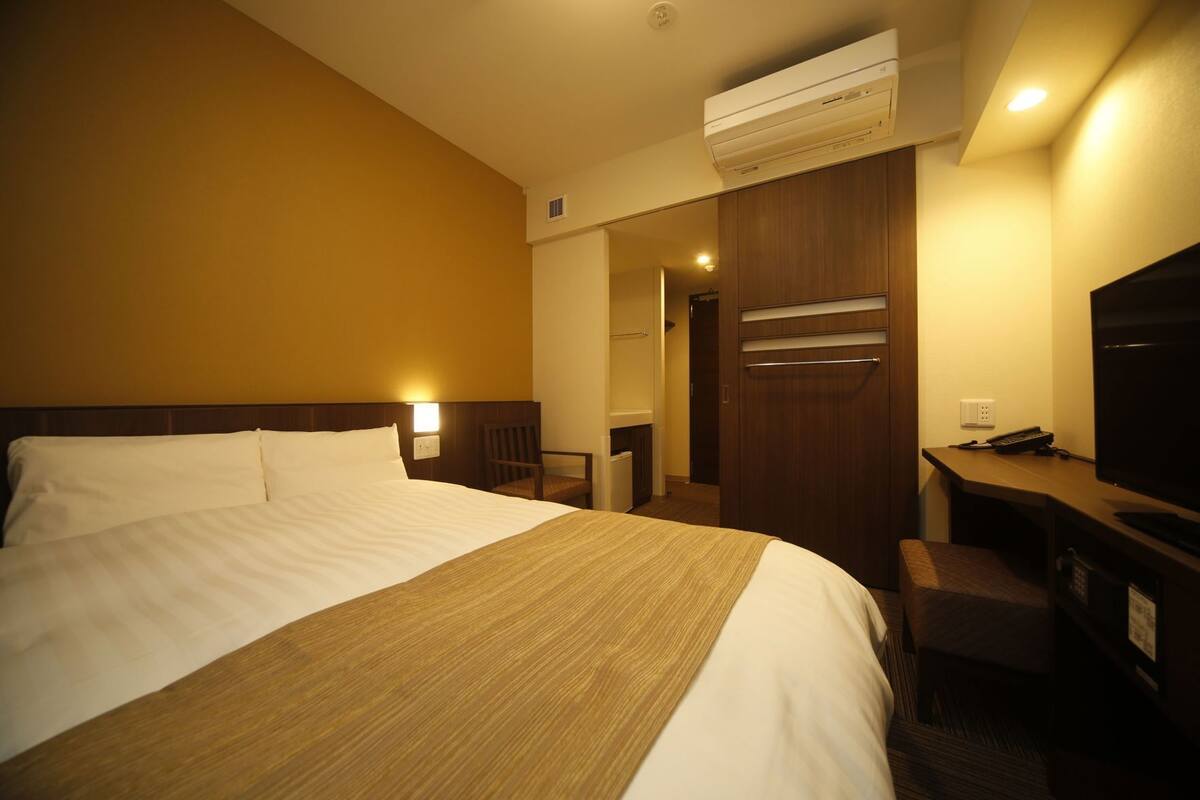 Ein Hotelzimmer mit einem großen Bett, einem Schreibtisch mit Stuhl, einem Fernseher und einer Klimaanlage.