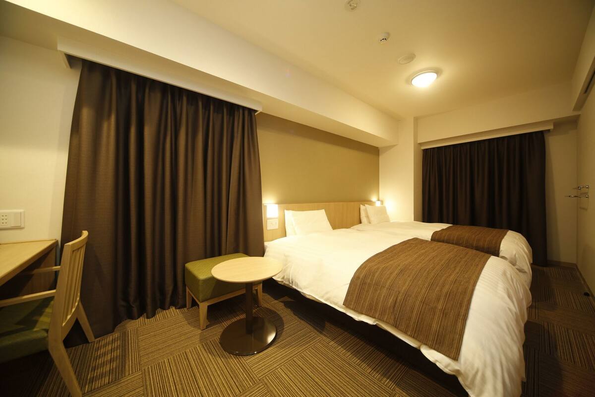 Ein Hotelzimmer mit Bett, Schreibtisch, Stuhl, kleinem Tisch und Teppichboden.