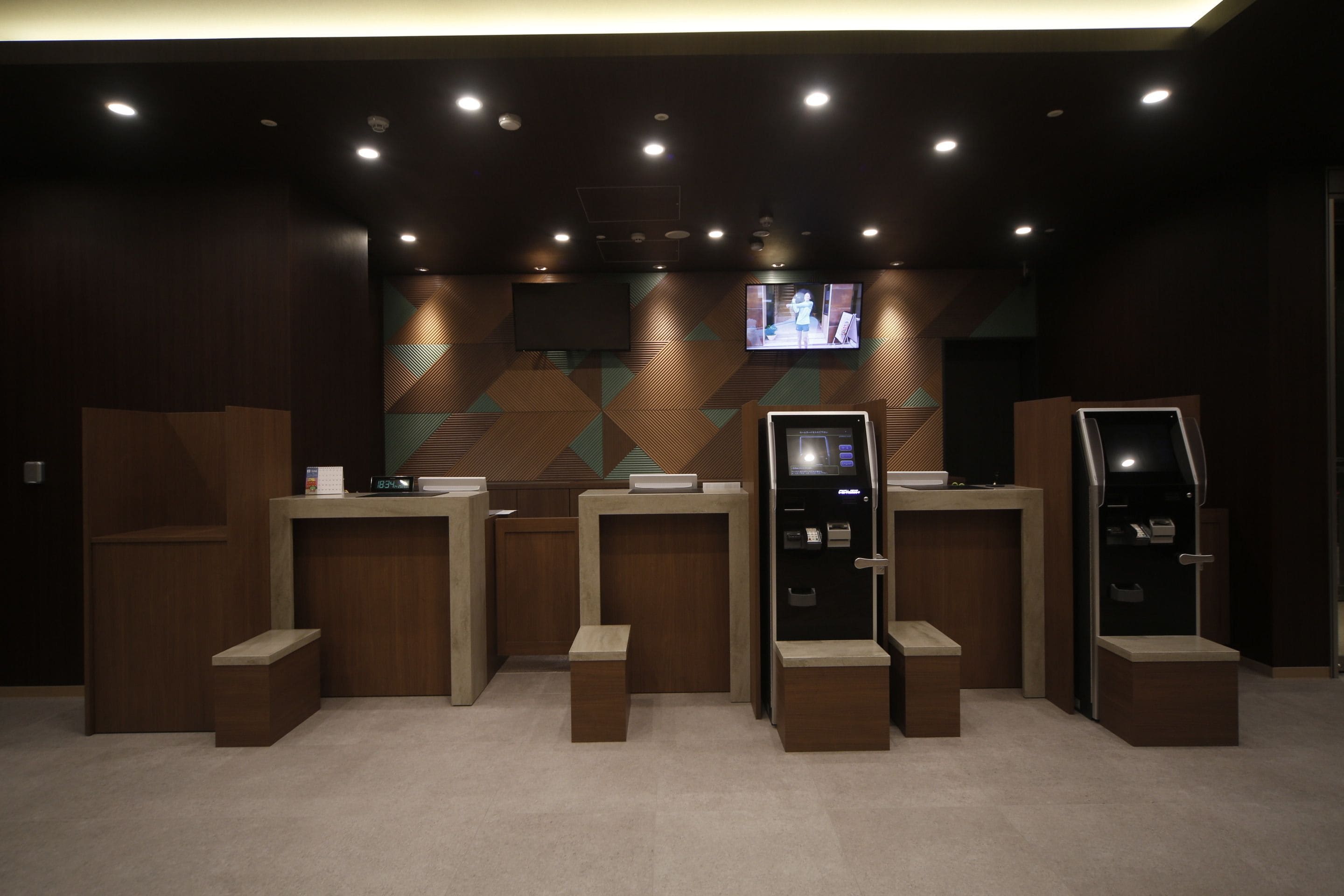A reception area with a modern design, featuring a reception desk, a television screen, and a self-service kiosk.