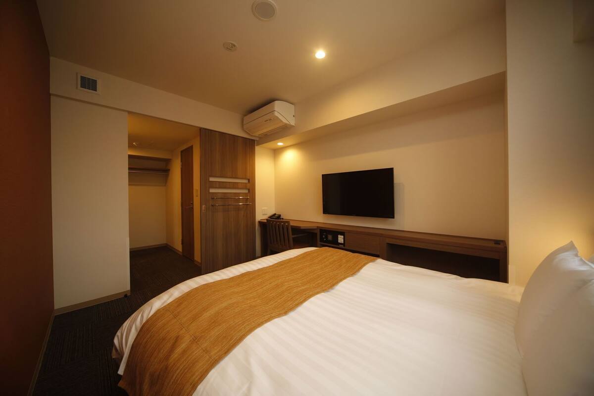 Ein Hotelzimmer mit Bett, Fernseher, Klimaanlage, Schreibtisch und Kleiderschrank.