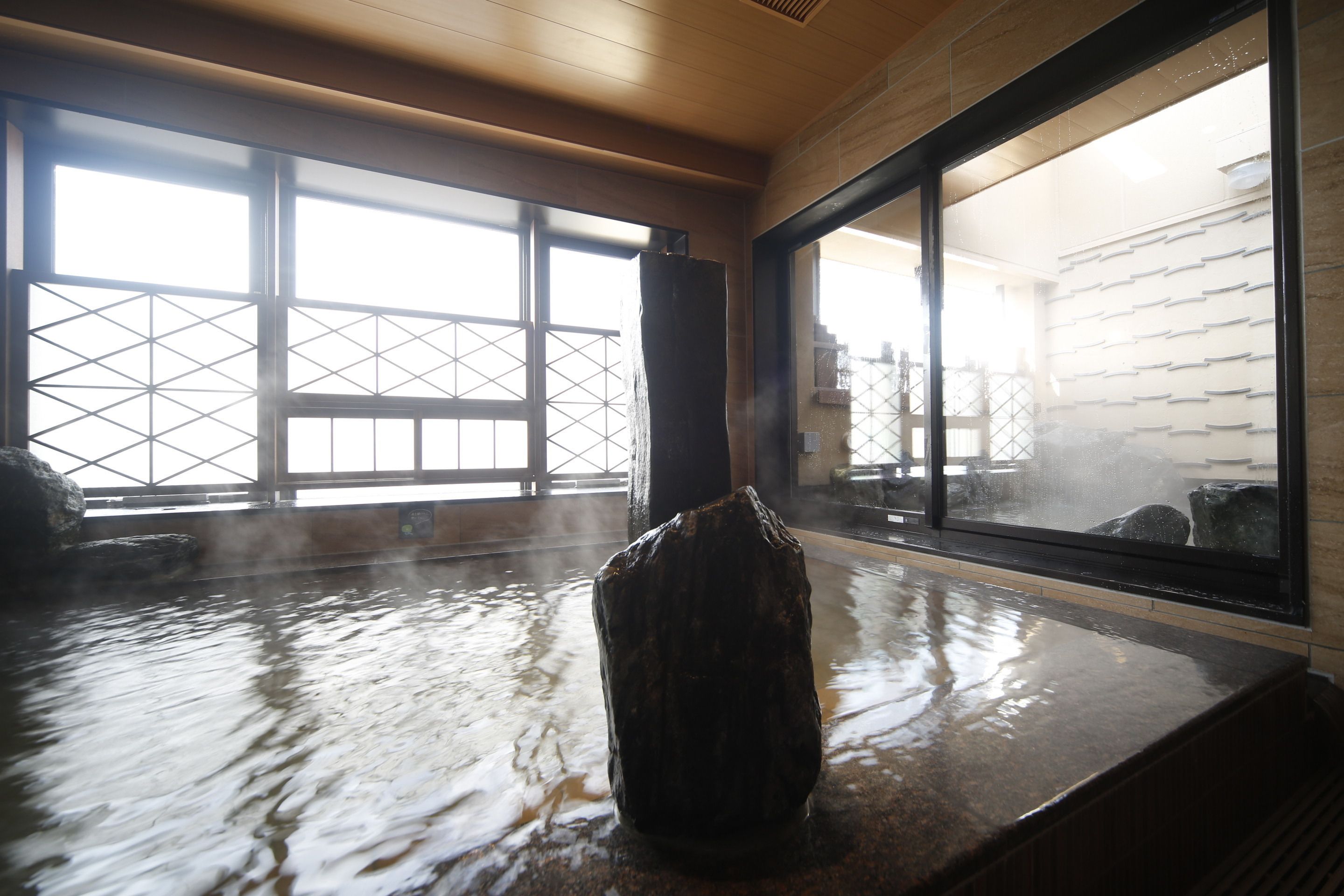 A hot spring area with a stone sculpture in the center, large windows, and a view of the outside.