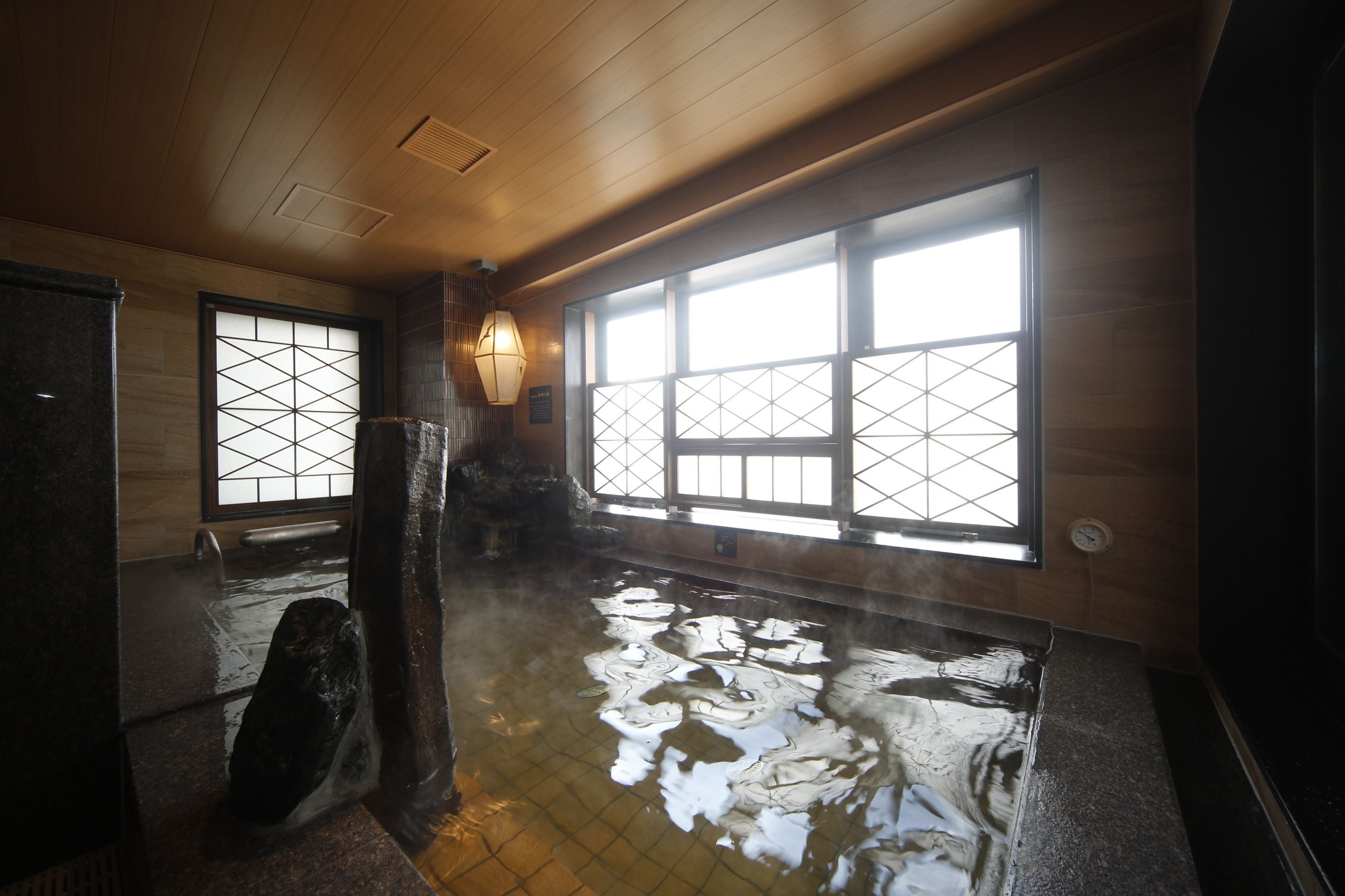 A traditional Japanese onsen with a wooden interior, large windows, and a stone basin.