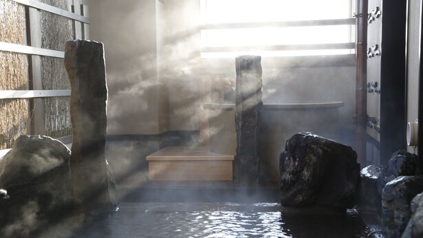 Un onsen japonais traditionnel, avec des plateformes en pierre et un mur en bois.