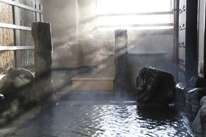 Ein traditionelles japanisches Onsen mit steinernen Plattformen und einer Holzwand.