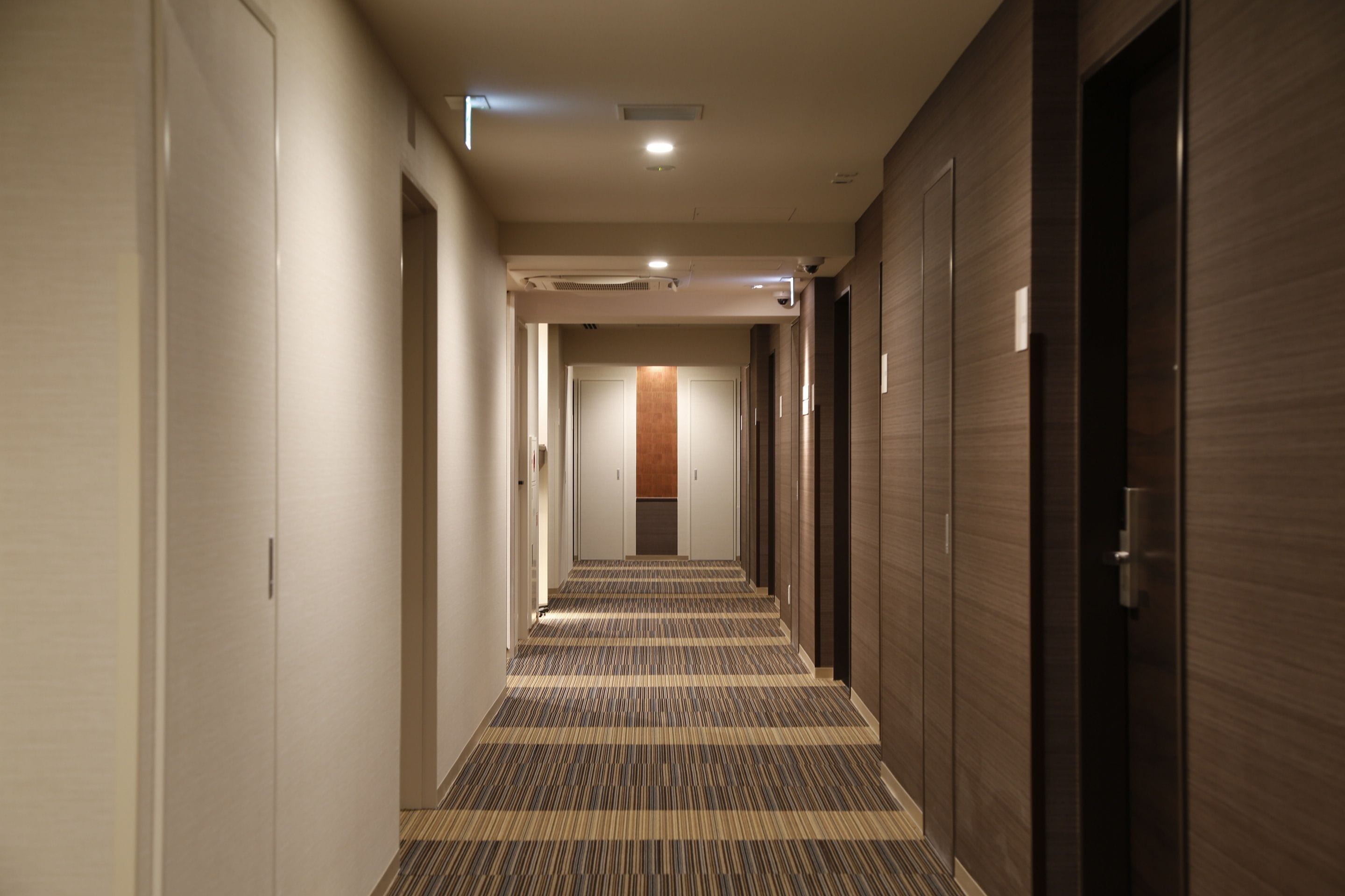 Een hotelgang met een kamergestreept tapijt, houten wanden en deuren die naar kamers leiden.