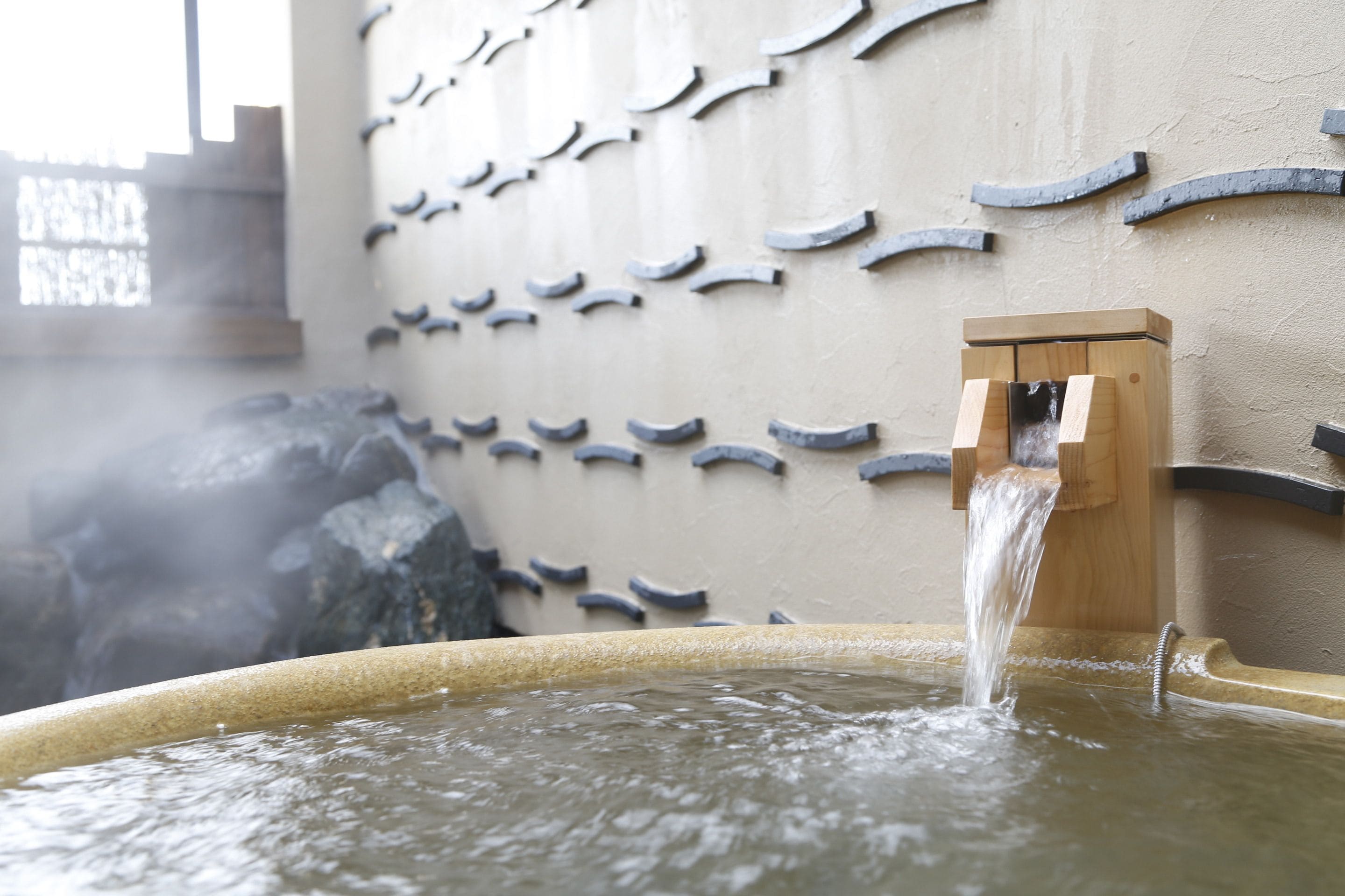 A hot spring with water flowing from a wooden spout into a stone basin.