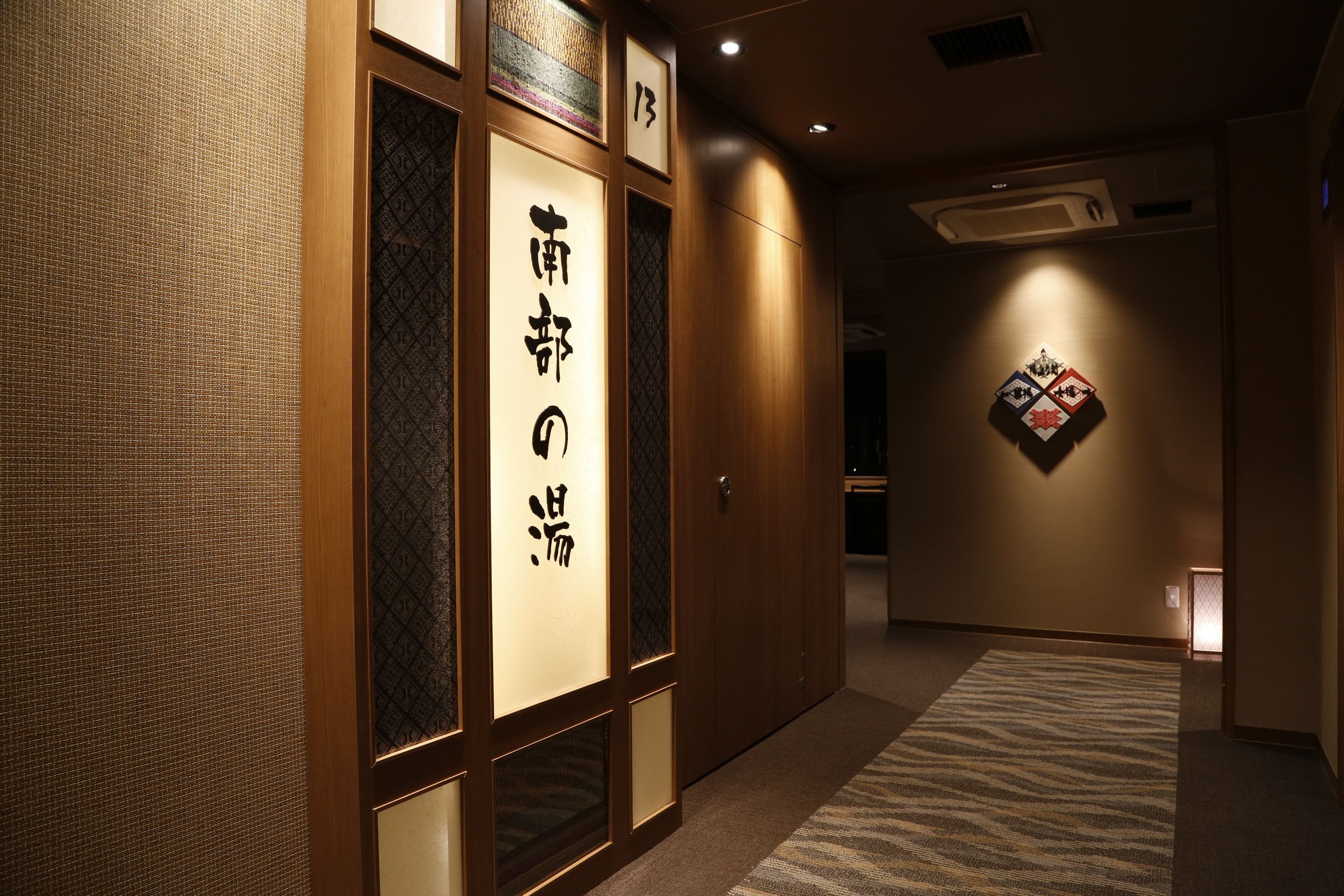 A hallway with traditional Japanese decor, including sliding doors with calligraphy, a patterned carpet, and a wall-mounted artwork.