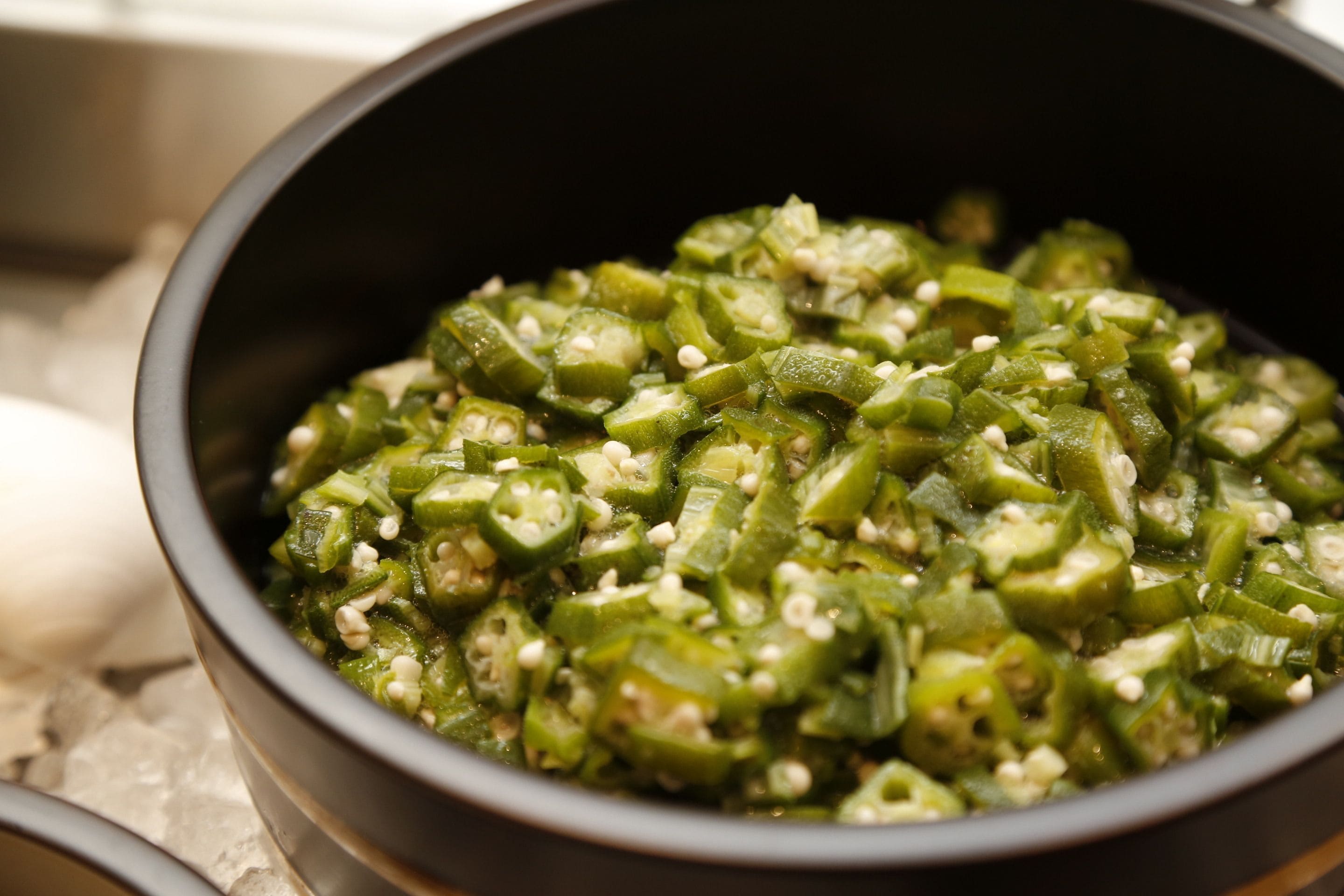 A bowl of sliced green vegetables, possibly okra, with seeds.
