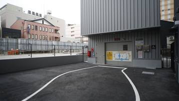 Un espace de stationnement extérieur avec une entrée de bâtiment, une zone délimitée par une clôture et un panneau d’affichage.